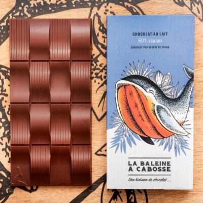 Tablette Chocolat au lait 50% de cacao de La Baleine à cabosse dans son emballage, posée à côté d'une tablette de chocolat au lai sans emballage
