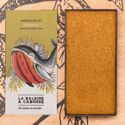 Tablette chocolat au lait 50% de cacao & bergamote de La Baleine à Cabosse dans son emballage posée à côté d'un moule en forme de tablette rempli de bergamote râpée