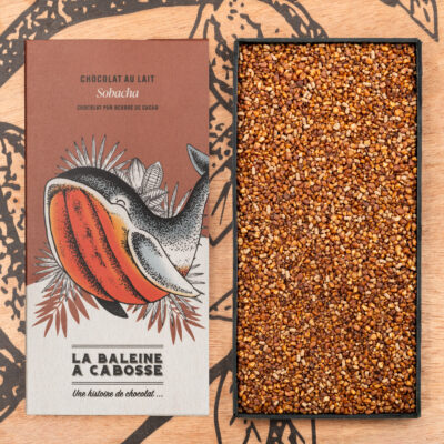 Tablette de chocolat au lait 50% de cacao & sarrasin grillé de La Baleine à Cabosse dans son emballage, posée à côté d'un moule en forme de tablette rempli de sarrasin grillé
