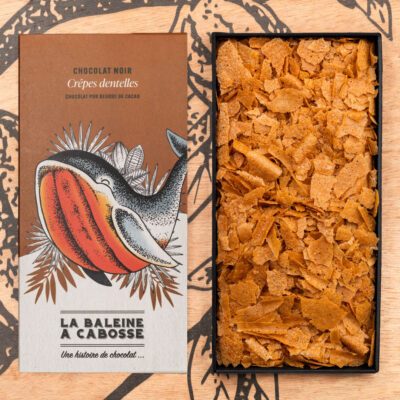 Tablette de chocolat noir 65% & crêpes dentelle de La Baleine à Cabosse dans son emballage, posée à côté d'un moule en forme de tablette rempli de crêpes dentelle