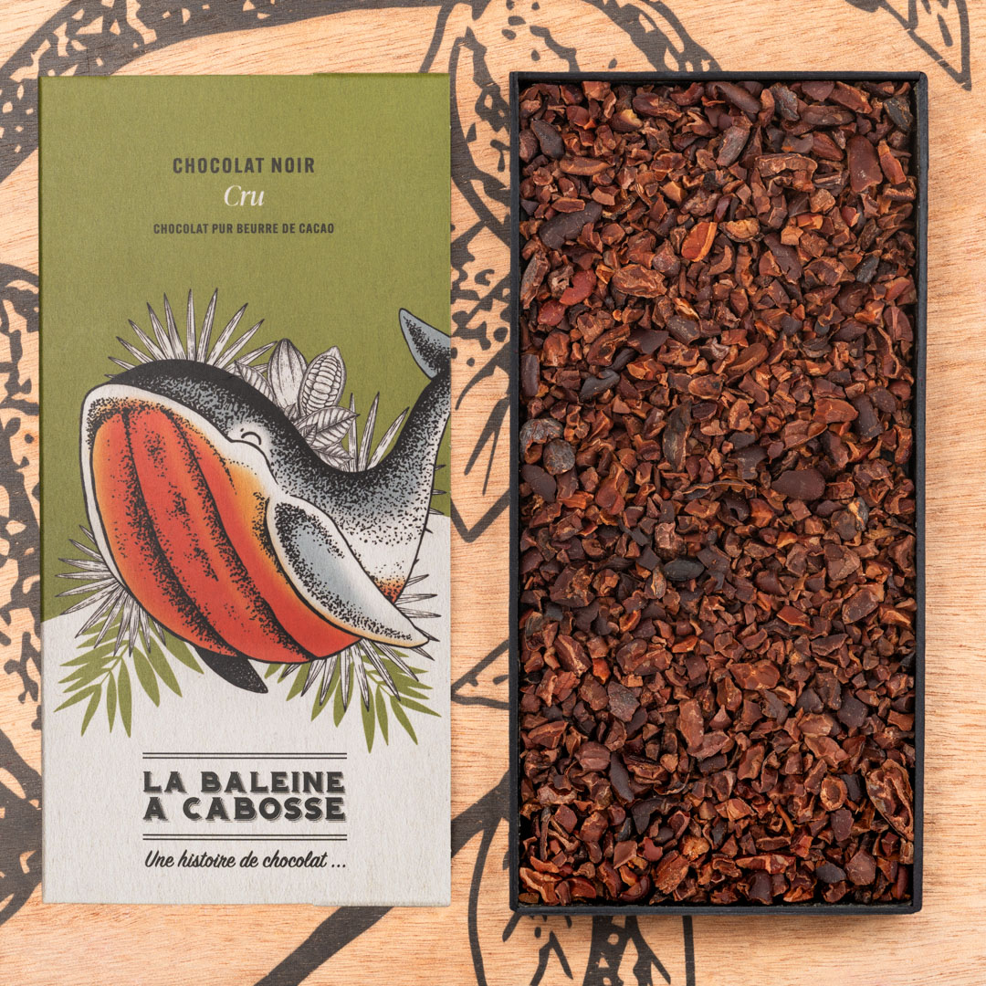 Tablette Chocolat Cru 76% 1 Tablette Chocolat Cru 76% de la Baleine à Cabosse dans son emballage, posée à côté d'un moule en forme de tablette rempli de grué de cacao