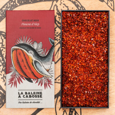 Tablette de chocolat noir 76% & piment d'Alep de La Baleine à Cabosse dans son emballage, posée à côté d'un moule en forme de tablette rempli de piment d'Alep séché