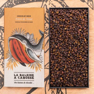 Tablette de chocolat noir 76% & poivre de timut de La Baleine à Cabosse dans son emballage, posée à côté d'un moule en forme de tablette rempli de grains de poivre de timut
