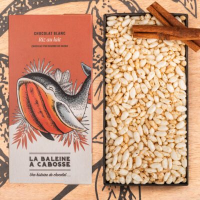 la tablette de chocolat blanc au riz au lait de La Baleine à Cabosse dans son emballage, posée à côté d’un moule en forme de tablette rempli de riz soufflé, avec deux bâtons de cannelle