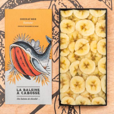 la tablette de chocolat noir 65% & banane de La Baleine à Cabosse dans son emballage, posée à côté d’un moule en forme de tablette rempli de rondelles de bananes