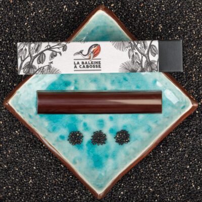 Barre fourrée au praliné de sésame noir posée à côté de son emballage sur une assiette bleue avec du sésame noir tout autour